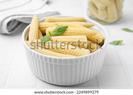 Canned baby corns with basil on white tiled table, closeup