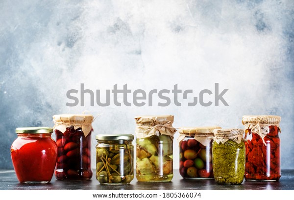 Canned\
food concept. Fermented, pickled, marinated preserved vegetarian\
italian snacks and sauces. Organic sun-dried tomatoes, artichokes,\
capers, olives, marinara sauces, pesto in jars\

