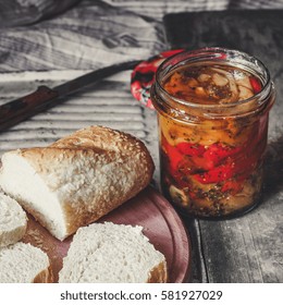 Canned peppers with bread on the kitchen board (antipasti) on the table