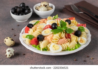 Canned Salmon Salad With Pasta, Cherry Tomatoes, Quail Eggs, Basil And Black Olives On Brown Background