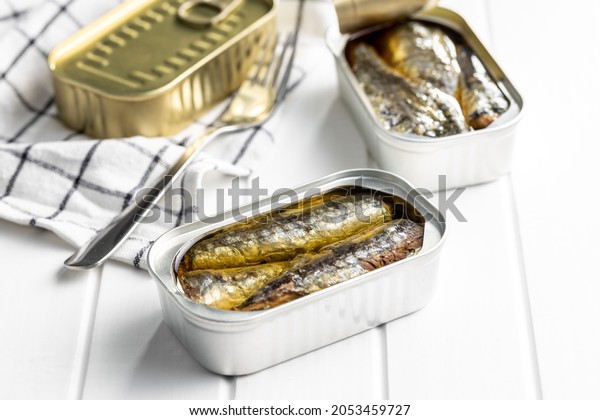 Canned sardines. Sea fish in tin can on white\
wooden table.