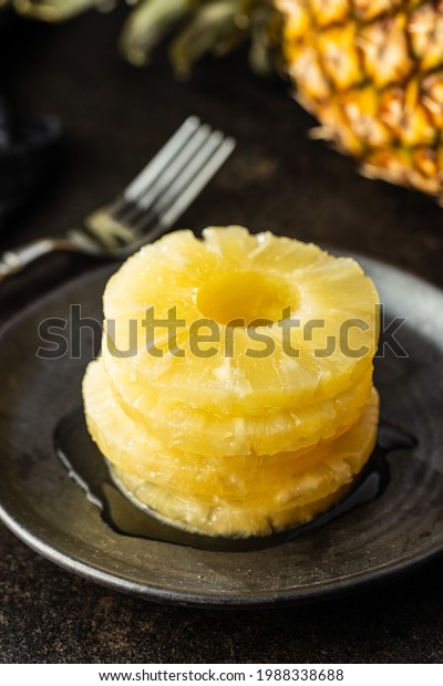 Canned\
sliced pineapple fruit on plate on black\
table.