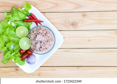 Canned Tuna In Glass Bowl With Fresh Vegetables Salad ( Tomato, Lemon, Red Chili Pepper, Red Onion ) On White Dish With Tuna Can On Wooden Table.