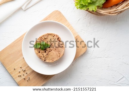 Canned tuna steak in brine on white plate on wooden table