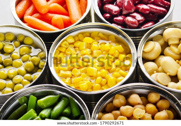 Canned vegetables in opened\
tin cans on kitchen table. Non-perishable long shelf life foods\
background