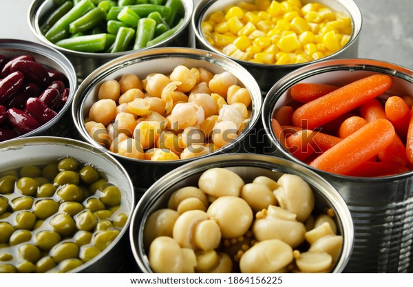 Canned vegetables in opened\
tin cans on kitchen table. Non-perishable long shelf life foods\
background