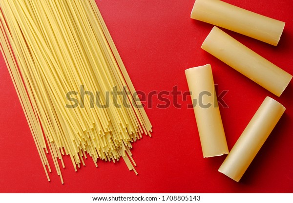 Cannelloni and spaghetti on a red background. Dry\
cannelloni tubules and spaghetti straws. Unprepared pasta. View\
from above. Selective\
focus.