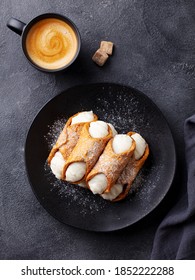 Cannoli Italian dessert on a plate with cup of coffee. Dark background. Close up. Top view.