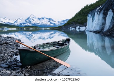 Canoe Resting On The Edge Of Valdez Glacier, Covered In Rock And Till (moraine) On The Lower Glacier Above Valdez Lake. Large Ice Cliff Of The Glacier And Icebergs Can Be Seen Beyond.