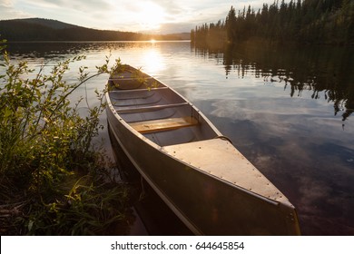 Canoe tied to shore of beautiful Frenchman Lake in remote wilderness of Yukon Territory, Canada, with sunset over boreal forest taiga framing the lake