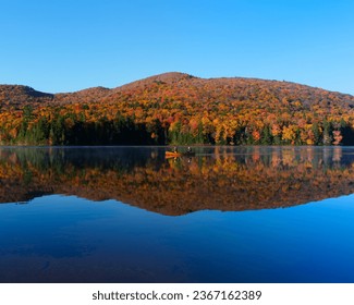 Canoe traveling on a mirror lake with autumn color mountain in the background over a blue sky and blue lake - Powered by Shutterstock