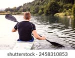 Canoeist man sitting in canoe holding paddle, in water. Concept of canoeing as dynamic and adventurous sport. Rear view, sportman looking at water surface, paddling