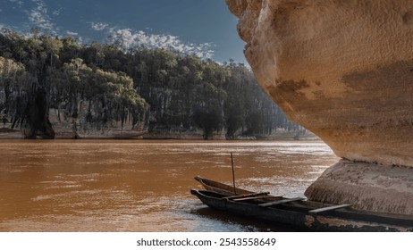 Canoes hollowed out of wood are moored at the entrance to the cave. The rock overhangs the red-brown river. Green vegetation on the far steep bank. Blue sky, clouds. Madagascar. Manambolo River - Powered by Shutterstock