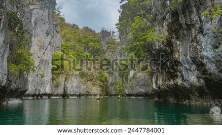 Canoes with tourists sail along a calm emerald lagoon surrounded by karst rocks. Green tropical vegetation on steep slopes. Reflection. Small lagoon. Philippines. Miniloc Island. Palawan