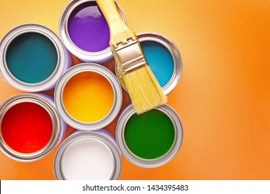 Cans of paints and brush on color background