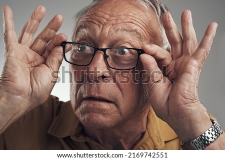 Cant believe what I just saw. Studio shot of an elderly man adjusting his spectacles against a grey background.