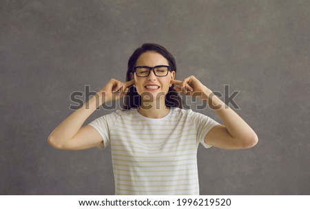 I can't hear you. Head shot of young woman in glasses closing eyes and plugging ears with fingers to ignore loud noise, unwanted opinion, dumb stupid comment or useless unsolicited uninvited criticism