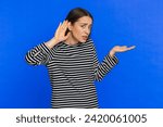 I cant hear you. What. Young Caucasian woman trying hear you looking confused and frowning keeping arm near ear for louder voice asking to repeat to hear information deafness. Girl on blue background