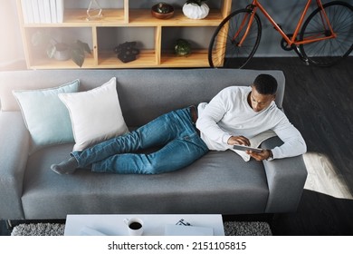 I Cant Manage To Find The App I Just Downloaded. High Angle Shot Of A Young Man Lying Down On A Couch And Using His Digital Tablet At Home.