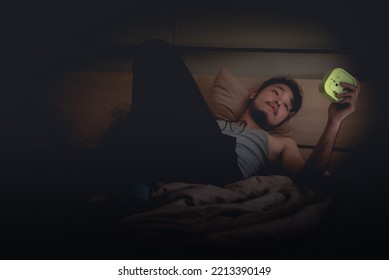 Can't Sleep At Nighttime Concept, Man Holding And Looking At Alarm Clock At Night On The Bed.