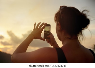 I cant wait to share this view. Shot of a young woman photographing a tropical view with her cellphone while on holiday.