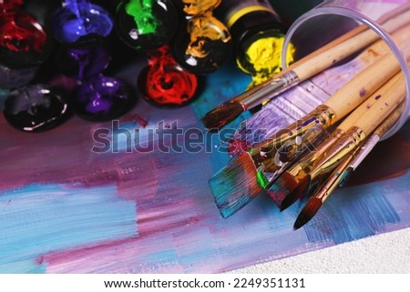 Canvas with colorful abstract painting and different brushes, closeup
