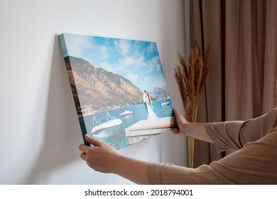 Canvas print with gallery wrap. Woman hangs wedding photography on white wall. Hands holding photo canvas print - Shutterstock ID 2018794001
