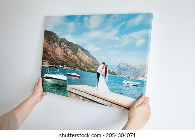 Canvas print with gallery wrap. Woman hangs wedding photography on white wall. Hands holding photo canvas print