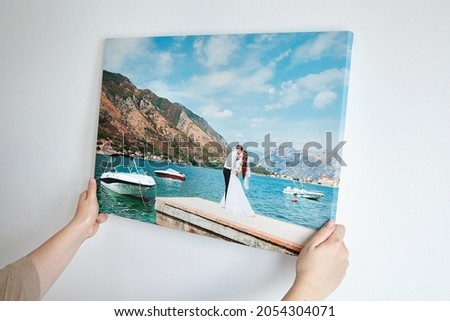 Canvas print with gallery wrap. Woman hangs wedding photography on white wall. Hands holding photo canvas print