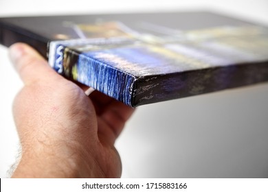 Canvas print. Hand holds a photo with gallery wrap method of canvas stretching on stretcher bar. Sample of stretched color photograph printed on canvas, lateral side, closeup.