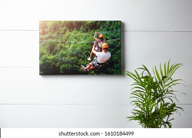 Canvas print. Photo hanging on a white wooden wall, front view. Green house plant and a color photography with image of people on zip line. Interior decor