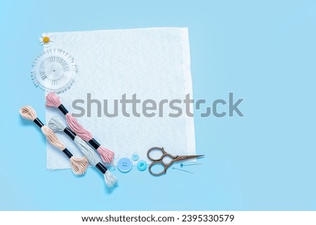 Canvas with scissors, mouline threads and ball pins on blue background