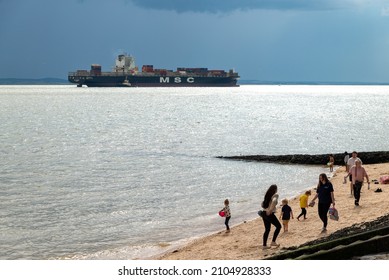 Canvey Island, Essex, UK - 31 July 2021: A Family Walks Along Canvey Beach As A Container Ship Sails Close By.