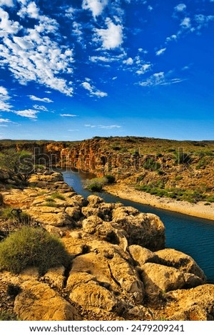 The canyon of the Yardie Creek in Cape Range National Park, Western Australia, with red and yellow limestone rocks and stunted outback vegetation
