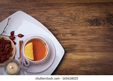 Cap Of Herbal Tea With Lemon And Raisins And Candle Flame On A Wooden Background