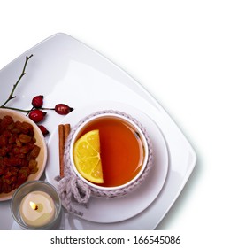 Cap Of Herbal Tea With Lemon And Raisins And Candle Flame On A White Background