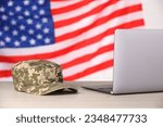 Cap and laptop on wooden table against flag of USA. Military education
