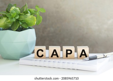 CAPA Corrective and Preventive action plans lettering on wooden cubes on the table next to a notebook and a flower in a pot