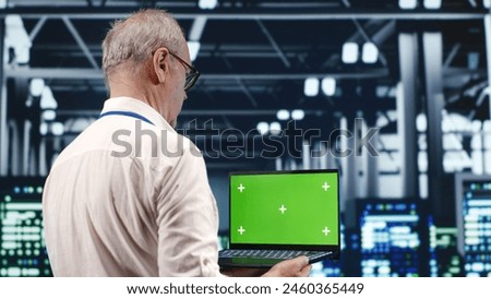 Capable IT professional navigating network of server clusters in industrial hub. Expert with green screen laptop ensuring proper operations, doing optimizations and maintenance in data center