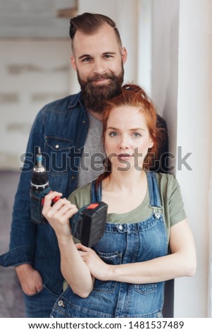 Capable young couple doing DIY renovations to their new home posing together with the woman holding an electric drill in her hand
