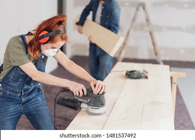 Capable young woman sanding planks of wood with an orbital sander in an unfinished room during DIY renovations - Powered by Shutterstock