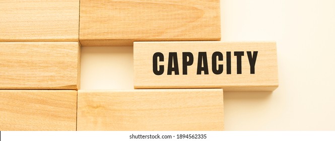 CAPACITY text on a strip of wood lying on a white table. Concept. - Shutterstock ID 1894562335