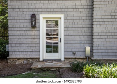 cape cod style home with white wood door at back entrance. Door has many glass windows and outside is an exterior light