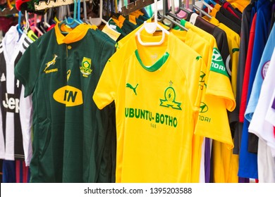 Cape Town - April 28, 2019: Springbok Rugby Supporters Team Shirts As Well As Soccer Or Football Shirts Of South African Local Team Hanging Up On Rails At A Street Market On Display