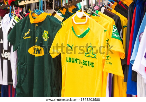 Cape\
Town - April 28, 2019: Springbok rugby supporters team shirts as\
well as soccer or football shirts of South African local team\
hanging up on rails at a street market on\
display