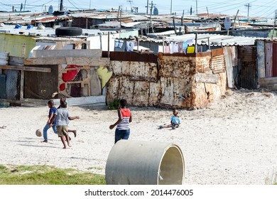 Cape Town - February 19, 2021:  children playing football or soccer in an African township in front of tin shacks concept daily life in Africa