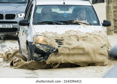 Cape Town - July 13, 2020:  Motor Vehicle Or Car Driving Through Sea Foam And Water On A Flooded Road After A Winter Storm With Selective Focus On The Front Of The Car Splashes Concept Road Safety