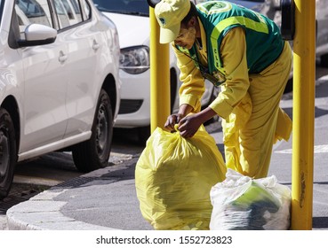 Cape Town - September 23, 2019:  Garbage Or Waste Collector, Sanitation Worker Or Lady Cleaning The Street And Putting Rubbish In Plastic Bags For Disposal, Tying A Knot In The Bag, Wearing Overalls