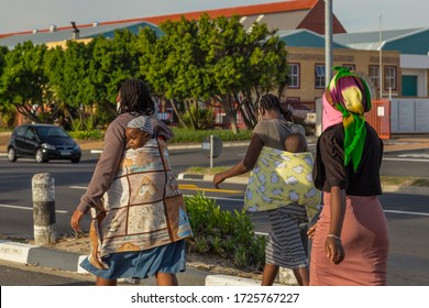 Cape Town, South Africa - 06 May 2020: African Woman Carrying Baby On Back, Wearing Face Mask During Covid 19 Corona Virus Pandemic, Trying To Survive Poverty And The Virus.