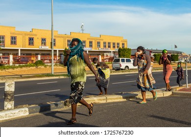 Cape Town, South Africa - 06 May 2020: African Woman Carrying Baby On Back, Wearing Face Mask During Covid 19 Corona Virus Pandemic, Trying To Survive Poverty And The Virus.